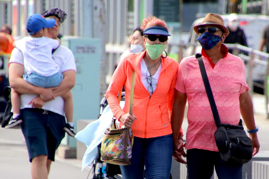 A couple dressed in bright clothing wearing face masks while walking on a busy footpath in Melbourne.