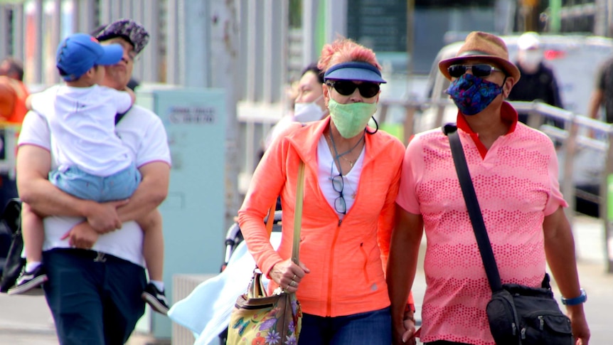 A couple dressed in bright clothing wearing face masks while walking on a busy footpath in Melbourne.