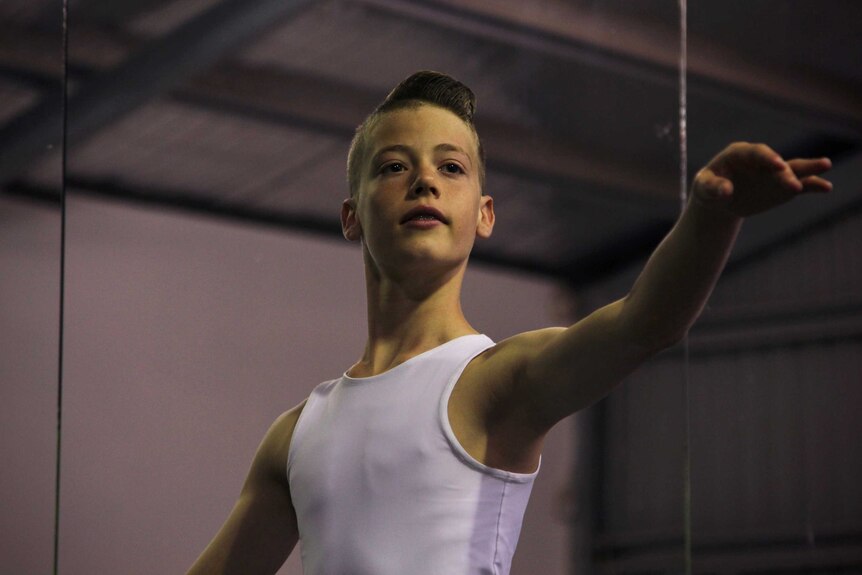 A boy in a ballet uniform practises.