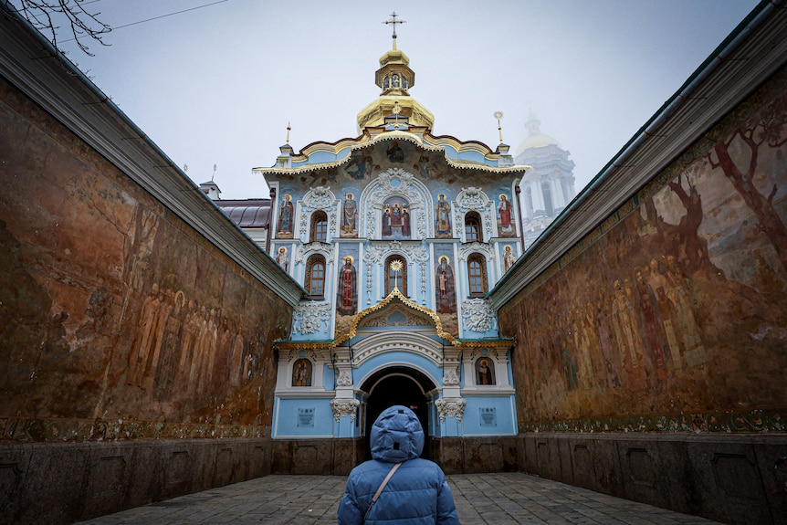 A woman in a blue coat looks up at an opulent gold and blue church
