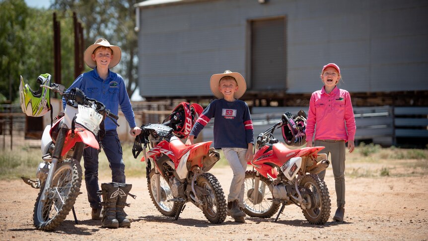 Three children stand beside their motorbikes