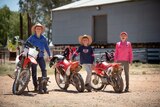Three children stand beside their motorbikes