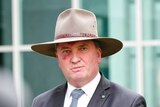 Barnaby Joyce listening to a question with his hands clasped during a press conference, wearing a broad-brimmed hat.