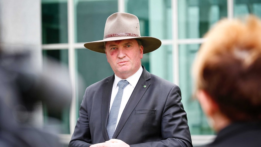 Barnaby Joyce listening to a question with his hands clasped during a press conference, wearing a broad-brimmed hat.