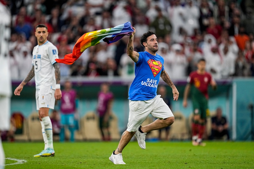 A man on a soccer field holding a rainbow flag