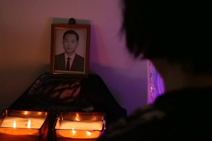 A woman looks at the black and white photo of a young man, with candles around.