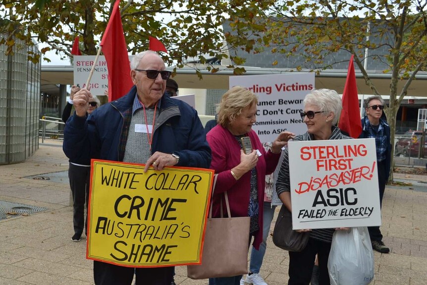 Several men and women hold placards saying things like: "White Collar Crime Australia's Shame".