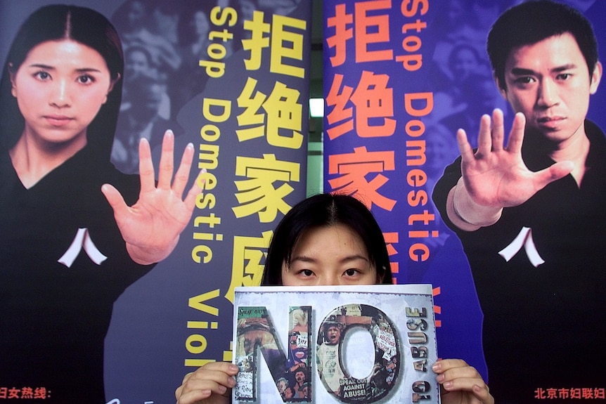 A Chinese girl holds a placard in front of a billboard during a campaign against domestic violence in Beijing. 