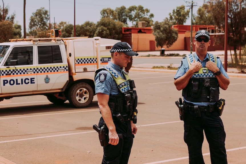 Two police officers standing near a police car in an outback town.