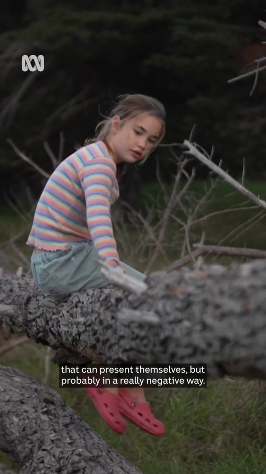 A girl with light-tone skin sits on a horizontal tree trunk