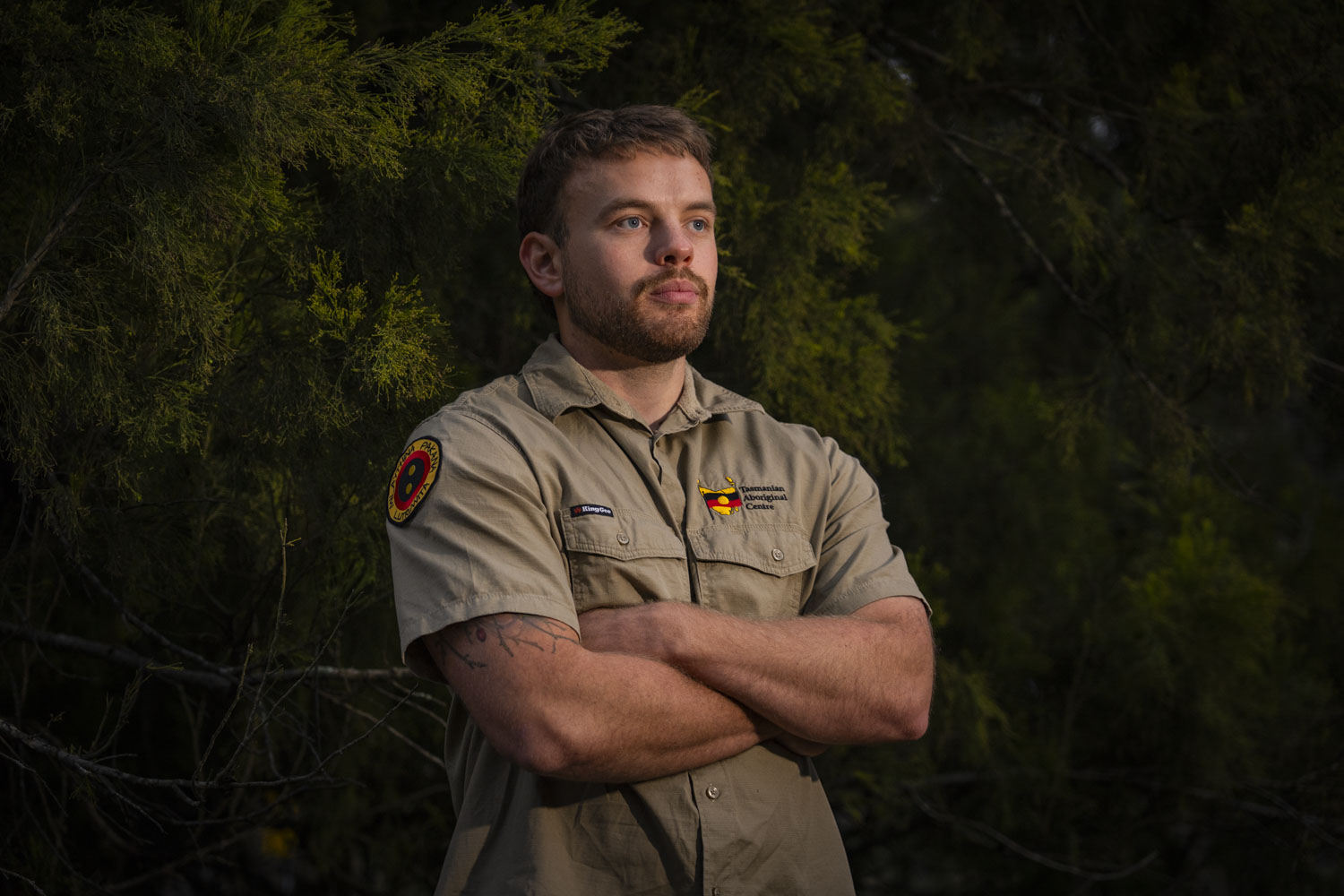 A man in a khaki shirt stands in the bush with a cherry tree behind him.