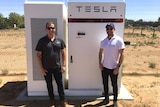 Two men smile at the camera with a box-y infrastructure behind them