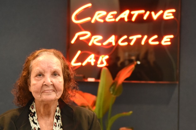 indigenous artist esme timbery stands in front of a sign that reads Creative Practice Lab, the artist died on october 6 2023