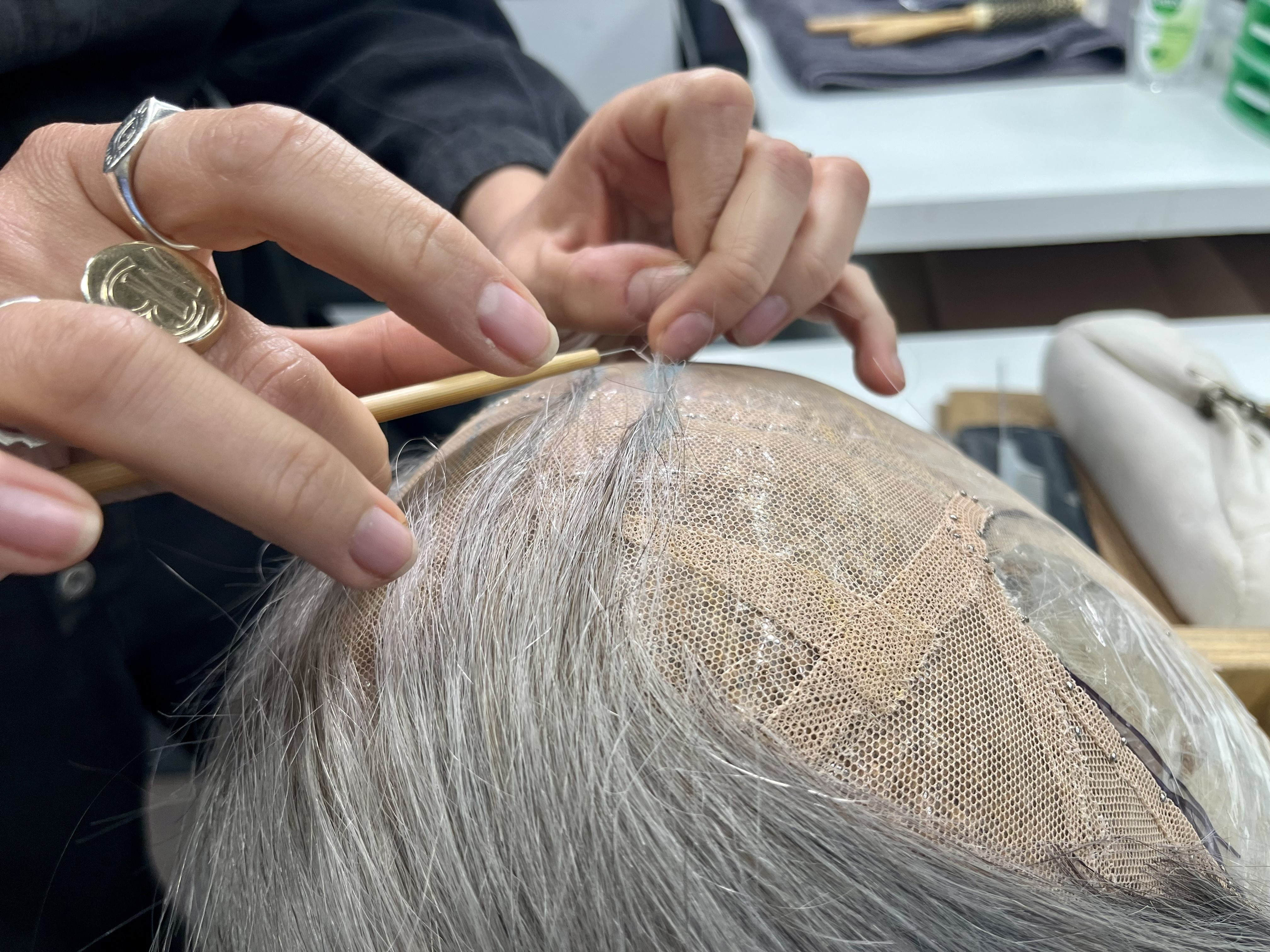 Hands stitching a grey wig