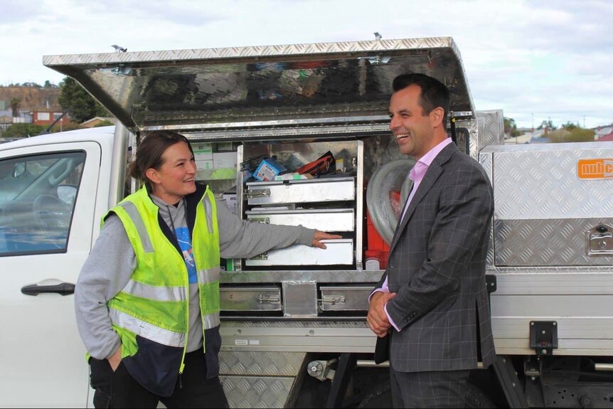 A woman and man laugh while next to a tradie ute.