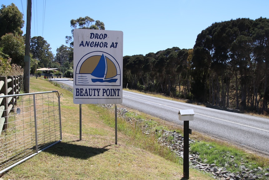 A sign reading 'Drop anchor at Beauty Point' stands on a grassy front lawn by the side of the road.