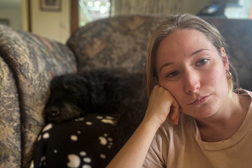 A young woman looking sad at the camera with her dog in the background