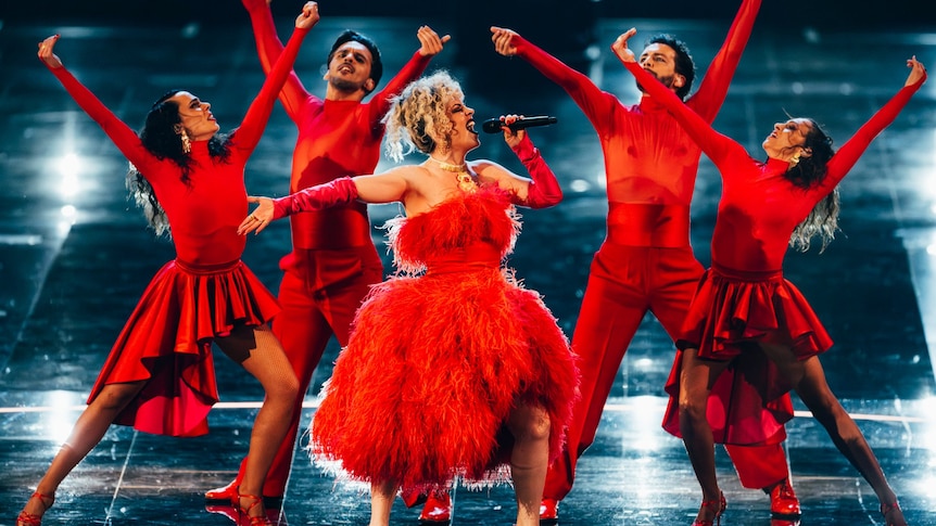 Five people dressed in red, the main person wearing a frilly dress, the others in skirts and pants with figure hugging shirts