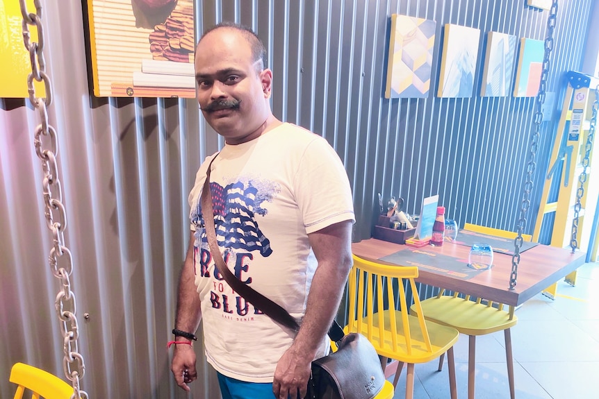 An man stands posing in a restaurant. 