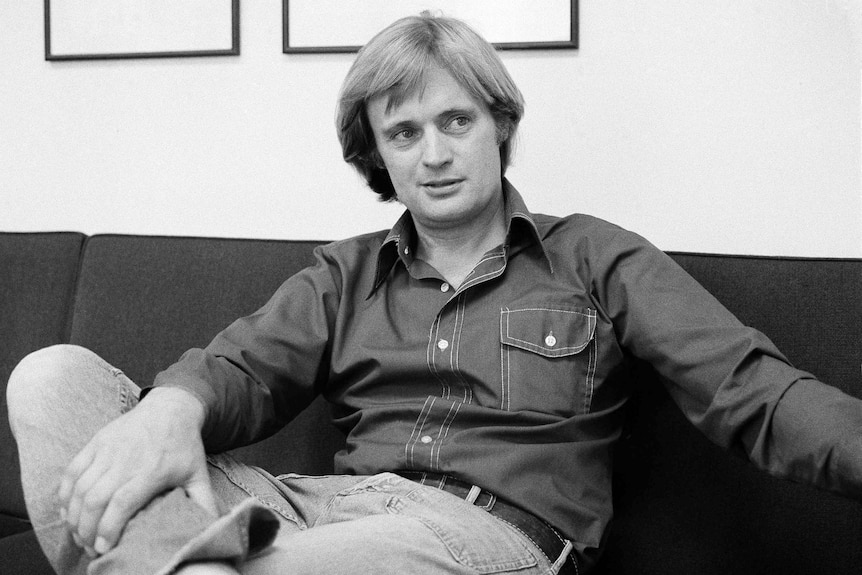 A young man sits on a couch in a black and white photo.