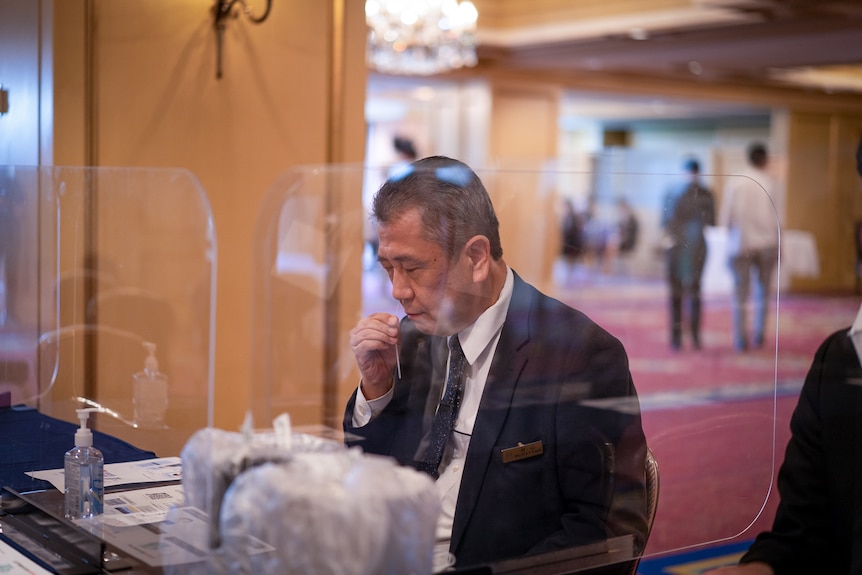 A Japanese man in a suit holds a plastic strip in his nostril 