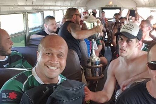 Rugby players on a bus celebrating victory with a trophy.