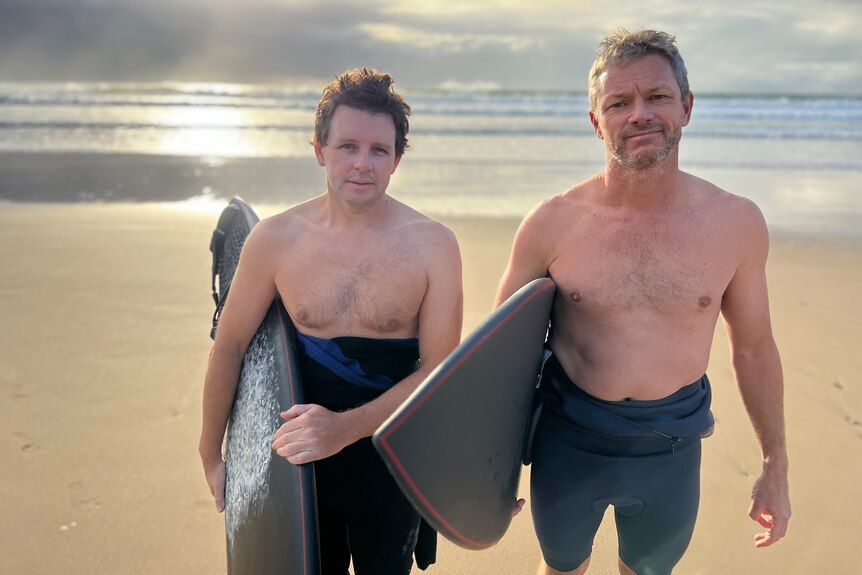 Two men in wetsuits with surfboards under their arms.