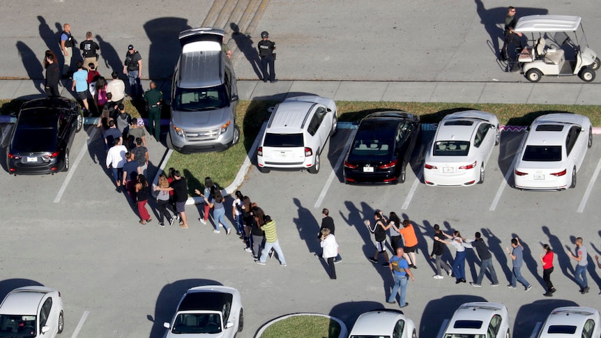 Students are evacuated in single file by police through a carpark