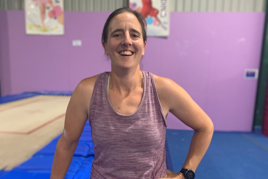 Goele Schmitz, in purple singlet, smiles in an indoor gymnastics space 