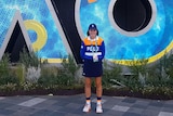 girl in ball kid uniform stands in front of AO sign
