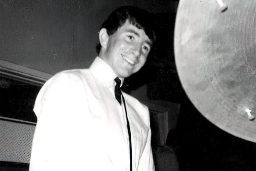 a black and white image of a teenager seated while wearing a high button-up shirt, smiling