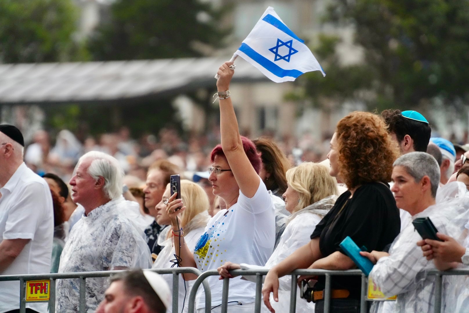 Uma mulher em um serviço memorial segurando uma bandeira israelense.