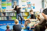 A young female drama student is acting out actions for a children's book being read by a fellow student.