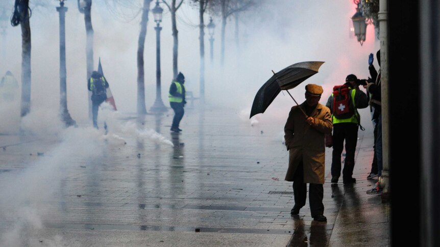 A man holding an umbrella makes his way through tear gas.