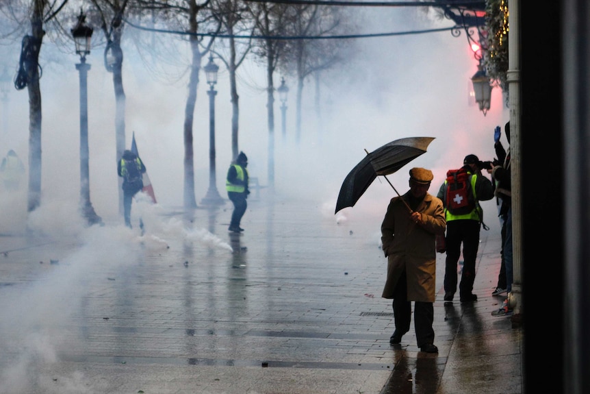 A man holding an umbrella makes his way through tear gas.