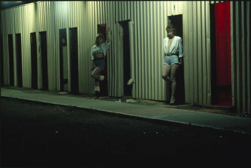 Prostitutes standing outside a brothel on a dark street.