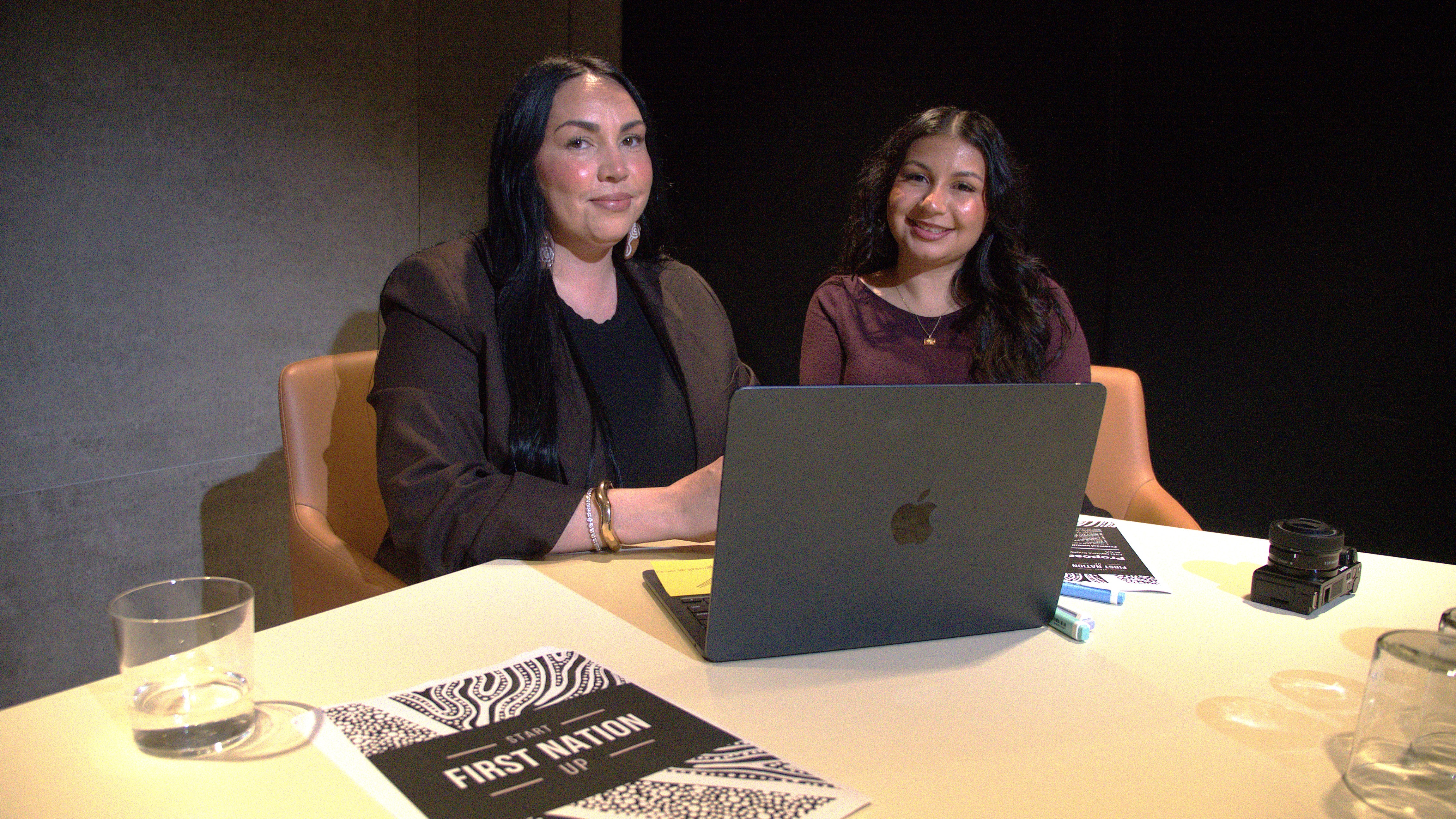 Sinead is sitting next to another woman at a desk with a laptop and paperwork in front of them