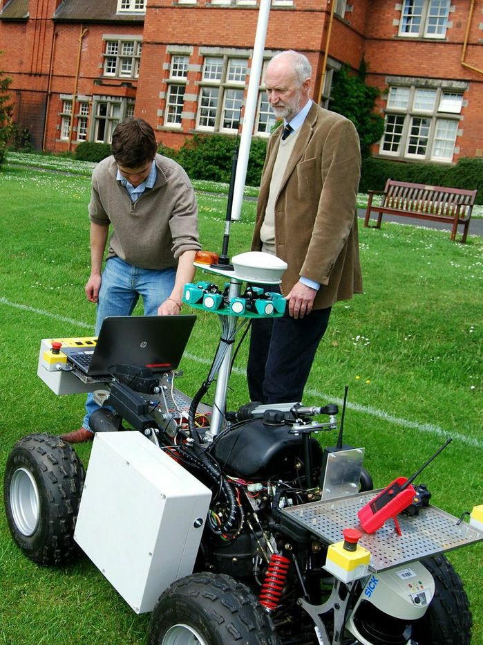 Professor Simon Blackmore looking at small trial robot on green grass at Harper Adams University, UK