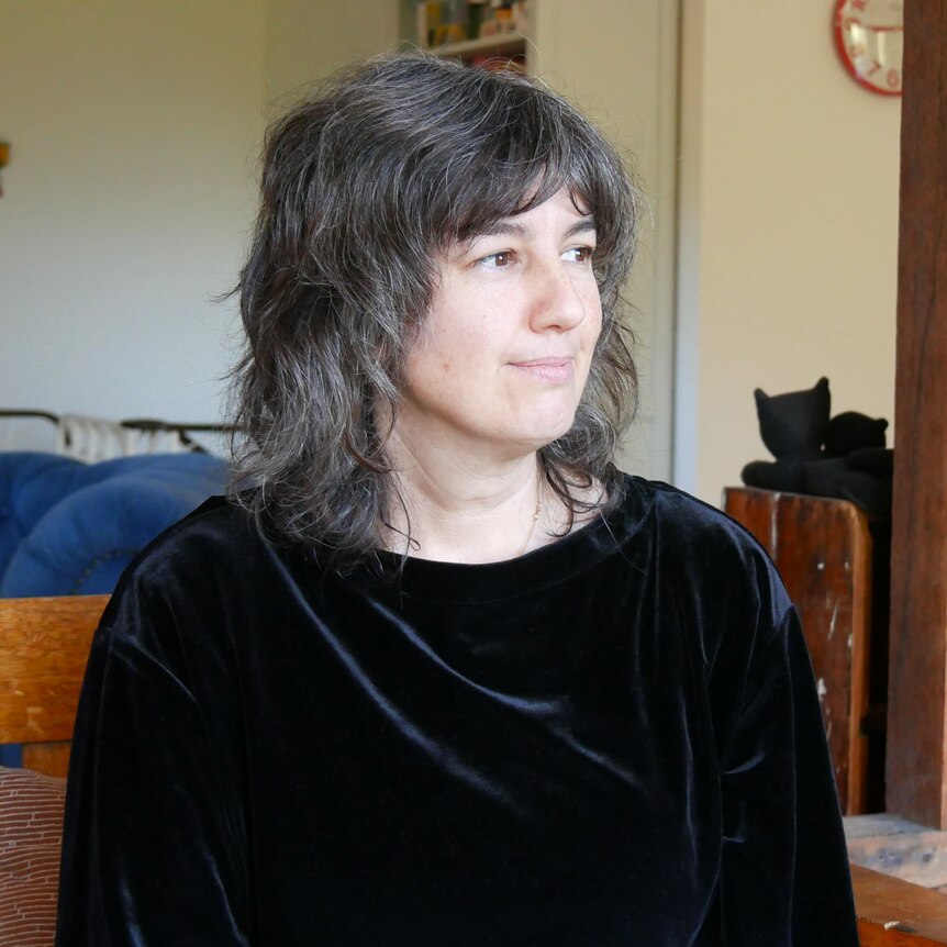 A woman wearing a black suede shirt looks into the distance with a slight smile. 