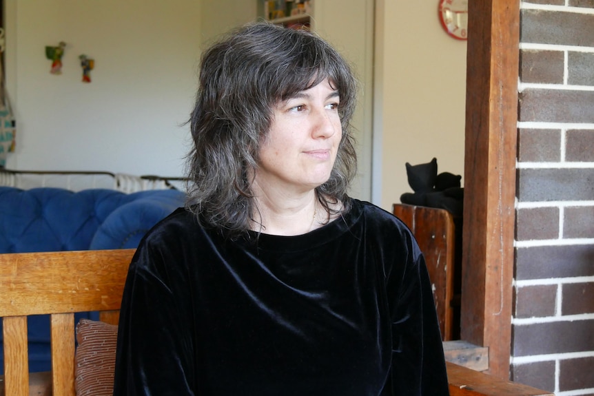 A woman wearing a black suede shirt looks into the distance with a slight smile. 