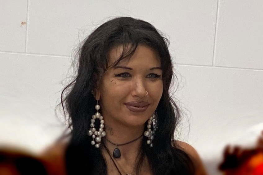 A woman wearing large earrings and necklaces smiles with two children seated on her lap