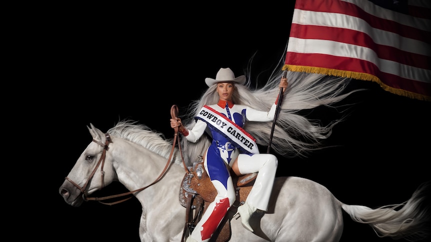 Beyonce on a white horse, carrying an American flag and wearing red, blue and white, with a white cowboy hat on