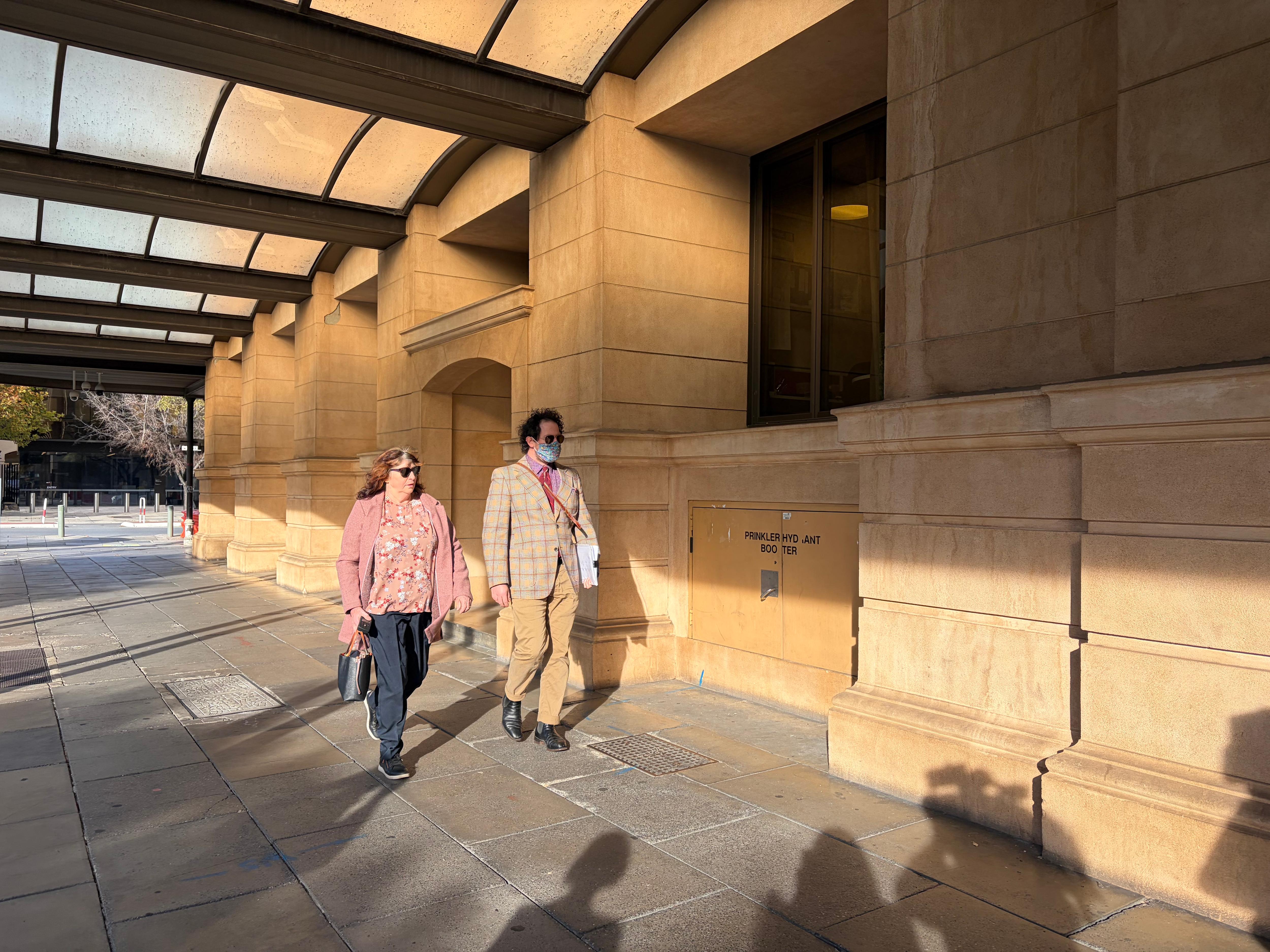 A woman wearing sunglasses walks along a footpath with a man.