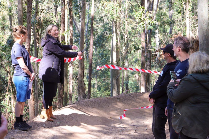 Emma McBride cutting red rape with scissor, smiling with a crowd looking on.