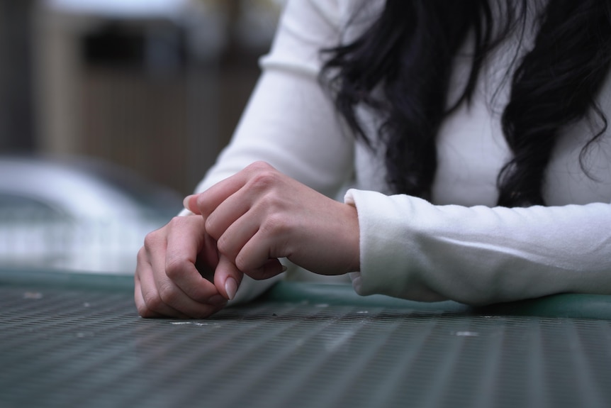 A woman's hands rest on a table.