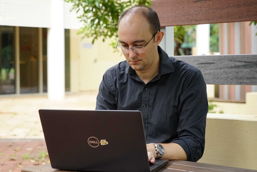 Charles Darwin University hydrogeologist Dylan Irvine sits outside working on a laptop.
