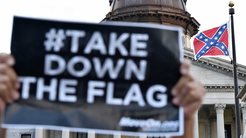 A #TakeDownThe Flag sign is held up in front of a Confederate Flag in South Carolina