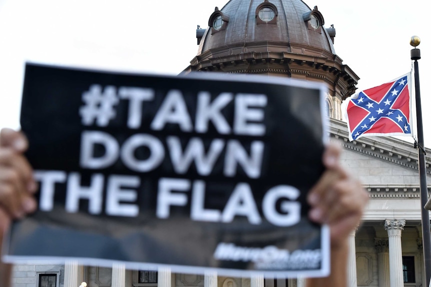 A #TakeDownThe Flag sign is held up in front of a Confederate Flag in South Carolina