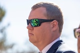A man looks straight ahead with green tinted sunglasses on