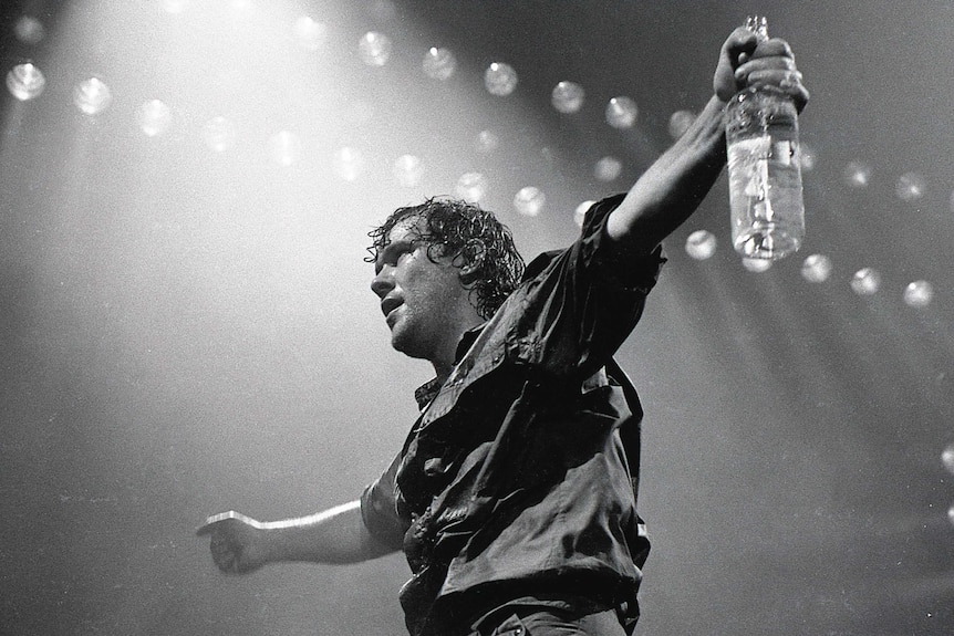 Black and white photo of Jimmy Barnes, with arms outstretched, performing at the Sydney Entertainment Centre.